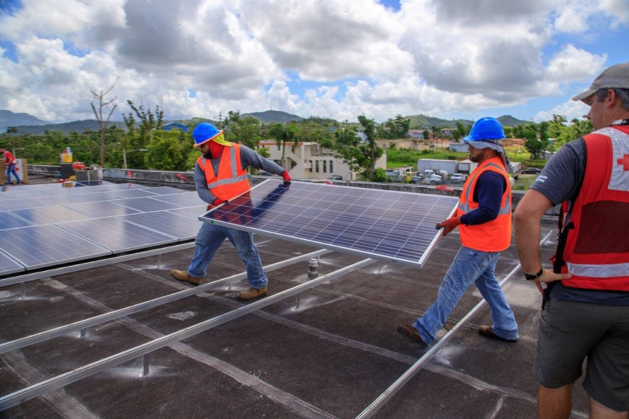 Técnicos instalando paneles solares en un techo con las montañas de Puerto Rico de fondo